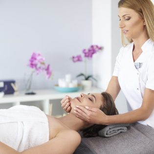 Kosmetikerin massiert das Gesicht einer entspannten Kundin während einer Beauty-Behandlung