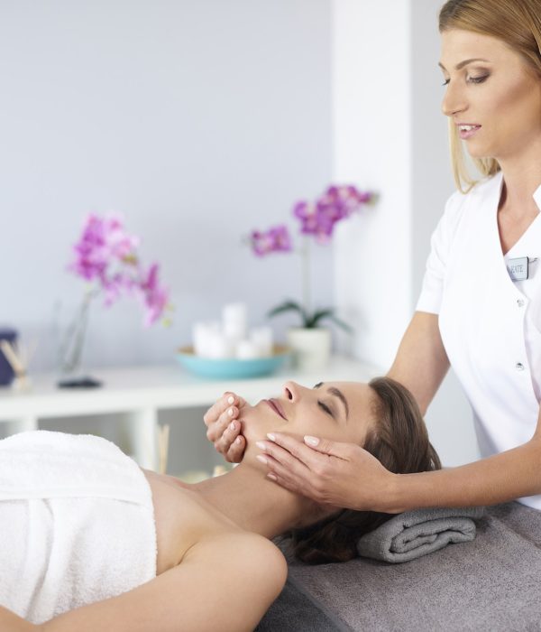 Kosmetikerin massiert das Gesicht einer entspannten Kundin während einer Beauty-Behandlung