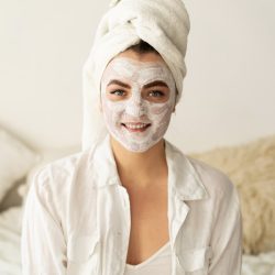 Frau mit Gesichtsmaske und Handtuch im Haar bei einer Beauty- und Hautpflegebehandlung