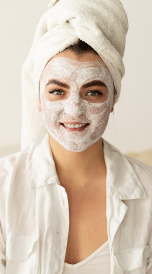 Frau mit Gesichtsmaske und Handtuch im Haar bei einer Beauty- und Hautpflegebehandlung